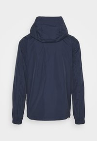 Veste à capuche bleu marine avec manches longues et poignets élastiques, vue de dos sur un fond clair uni.