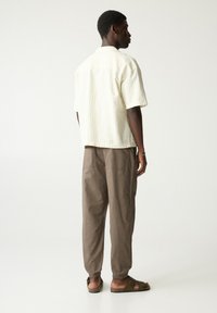 Korte mouw, off-white shirt met subtiele verticale strepen, gecombineerd met bruine, losse broek en bruine sandalen, weergegeven van achter.