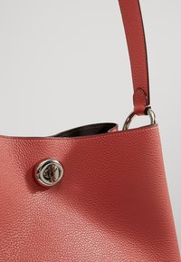 Sac à main en cuir rouge texturé avec fermeture à verrou argenté et bandoulière attachée sur un fond clair uni.