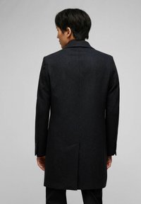 Schwarzer Wollmantel mit tailliertem Schnitt, Reverskragen und Schlitzen hinten. Strukturiertem Stoff mit glatter Oberfläche.
