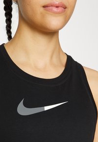 Camiseta atlética sin mangas negra de algodón, con un gran logo de Nike en gris y blanco en el pecho. Textura suave, escote redondeado.