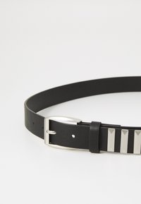 Ceinture en cuir noir avec une boucle en métal argenté. Présente des accents argentés rectangulaires sur la sangle. Texture lisse avec des trous perforés pour le réglage de la taille.