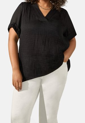 Schwarze Bluse mit V-Ausschnitt, kurzen umgeschlagenen Ärmeln und strukturiertem Stoff. Kombiniert mit weißen Hosen, die eine lässige Passform zeigen.