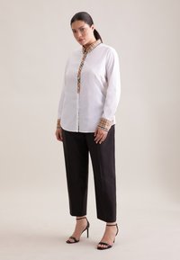 Weißes Hemd mit Knopfleiste, mit beigen karierten Kragen und Ärmelmanschetten, kombiniert mit schwarzen, maßgeschneiderten Hosen und schwarzen Riemchenabsätzen.