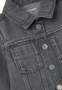 Chaqueta de mezclilla gris con un collar clásico, botones de metal plateado, dos bolsillos frontales y una fila de strass a lo largo del canesú.
