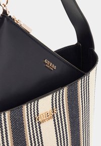 Borsa a tote in tela a righe nei colori beige, navy e crema; dettagli in logo dorato; fodera nera liscia; chiusura con zip; spallacci per un facile trasporto.