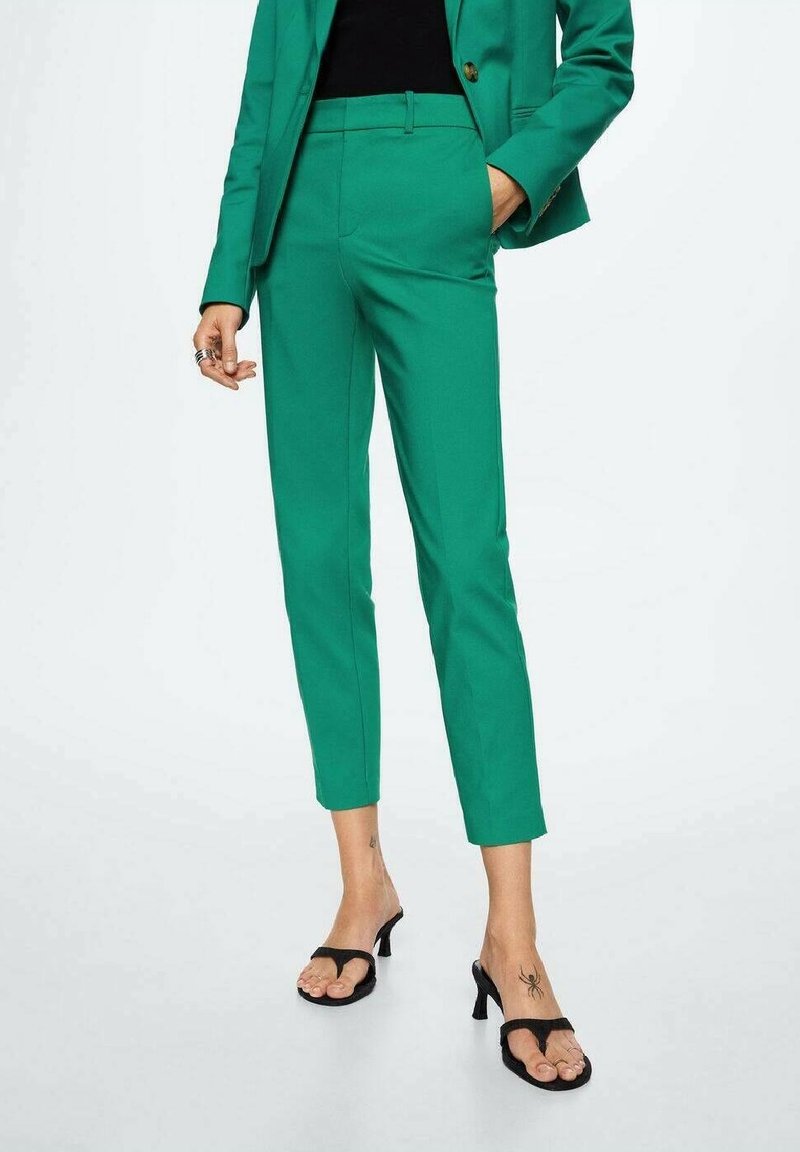 Pantalons ajustés verts avec une coupe slim, texture lisse et longueur raccourcie, associés à des sandales noires à lanières.