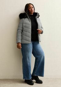 Zwart-wit houndstooth pufferjack met een nepbont capuchon, gecombineerd met wijduitlopende blauwe jeans en zwarte platform laarzen.