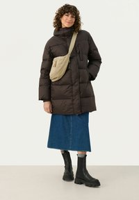 Brown puffer jacket with a high collar and a side pocket, paired with a denim skirt and black chunky heeled boots. Beige crossbody bag.