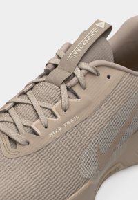 Béžová bežecká trailová obuv Nike s vrchným dielom z priedušnej sieťoviny, detailnými šnúrkami a štítkom s nápisom "Juniper Trail" na jazyku.