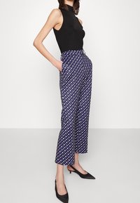 Pantalones de patrón marino con diamantes blancos y lavanda, de corte cropped, con bolsillos laterales, combinados con una blusa sin mangas negra y tacones negros.