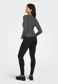 Maglietta nera a maniche lunghe con grandi pois bianchi, forma aderente, abbinata a jeans skinny neri e scarpe nere con suola spessa, vista da dietro.