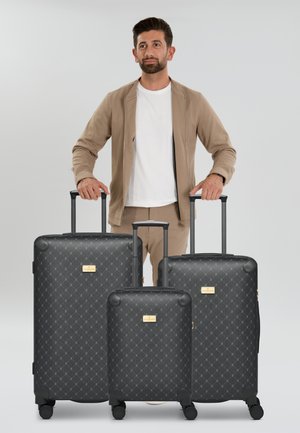Three black patterned suitcases with gold accents, varying in size, feature a textured exterior and retractable handles, resting on wheels.