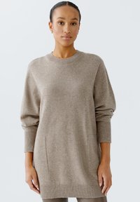 Hellbrauner, oversized Pullover aus weichem Material mit langen Ärmeln, gerippten Bündchen und Saum sowie zwei seitlichen Taschen.