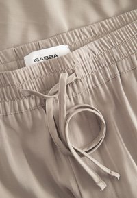 Vaaleanbeiget, joustavat shortsit, joissa on kiristysnyöri ja sileä pinta. Vyötäröllä näkyy GABBA-merkkilappu.