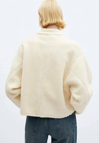 Giacca in pile morbido color crema, con un design cropped e maniche oversize. Presenta un colletto alto e dettagli di cucitura discreti.