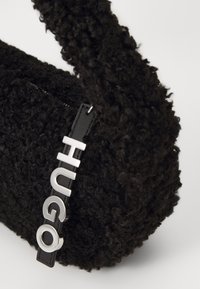 Svart teksturert håndveske laget av krøllet stoff, med en elegant stropp og en sølvfarget logoakcent på en svart lærtag.