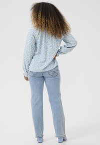 Helles blaues Blusenshirt mit langen Ärmeln und lässiger Passform, kombiniert mit hellblauen geraden Jeans. Das Shirt hat geraffte Manschetten und eine Rückenpasse.