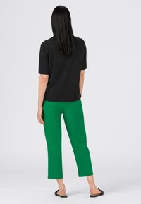 Haut noir à manches courtes et pantalon vert à jambes larges. L'ensemble présente une coupe décontractée avec une texture lisse, complété par des sandales plates noires.
