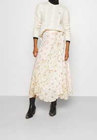 Blomster maxi-nederdel i creme med pastelfarvede blomster, en flydende silhuet og en lagdelt kant; sammen med en chunky creme striktrøje og sorte støvler.