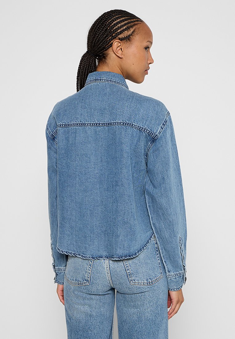 Spijkerjack in lichtblauw met een relaxte pasvorm. Beschikt over een puntige kraag, lange mouwen en gestikte details langs de naden.