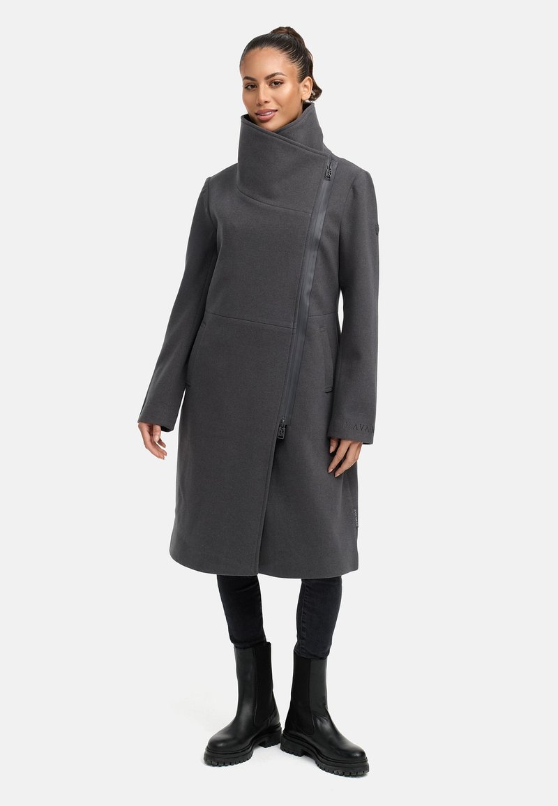 Mörkgrå ullkappa med hög krage, asymmetrisk dragkedja fram och långa ärmar. Stylad med svarta byxor och kraftiga stövlar.