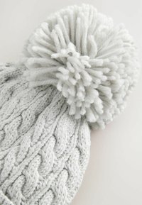 Grijze gebreide beanie met een gestructureerd kabelpatroon, afgewerkt met een pluizige pompon van zacht garen.