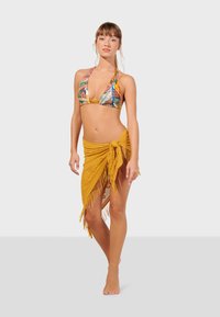 Pestrý bikini s dizajnom s halter výstrihom, v kombinácii s etno sukňou s frnčami v horčičovej farbe, previazanou okolo pása. Hladká textúra a žiarivé vzory sú evidentné.
