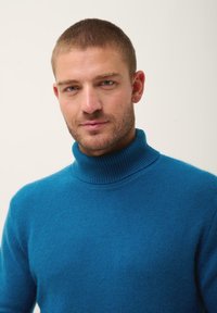 Maglione turtleneck in lana turchese con colletto a costine e una texture morbida, caratterizzato da un design aderente e maniche lunghe.