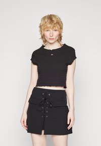Sort cropped top med en tekstureret, smocked design og frynsede kanter. Sættes sammen med en sort nederdel med snørebånd foran og lommedetaljer.