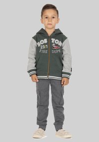 Ritssluiting hoodie met groene romp en grijze mouwen, met de tekst "BOSTON FIRE DEPT" en een afbeelding van een brandweerauto. Gecombineerd met grijze cargobroek.
