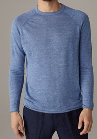 Chemise bleue à manches longues en tissu texturé avec un col rond et des manches raglan, présentant un motif chiné subtil.