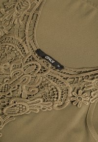 Haut vert olive avec des détails de broderie en dentelle complexe au niveau de l'encolure. Texture lisse, présentant une étiquette de marque indiquant la taille 36.