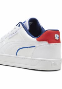 Sneaker in pelle bianca con accenti blu e un tab di rosso sul tallone. Presenta un badge con logo blu e una suola in gomma testurizzata con branding.