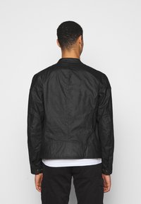 Czarna bomberka o fakturowanej powierzchni, z okrągłym kołnierzem, długimi rękawami i dopasowanym krojem. Widoczne szwy i subtelne detale przeszyć.