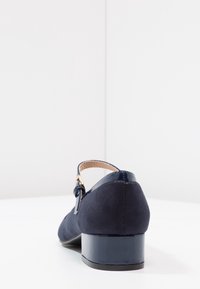 Scarpa in camoscio blu navy con punta arrotondata, tacco basso a blocco e cinturino alla caviglia con fibbia in metallo dorato. Dettagli in pelle verniciata liscia.