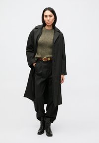 Μαύρο μακρύ παλτό, πουλόβερ πλεκτό σε ελιά, μαύρο παντελόνι με ψηλή μέση, καφέ ζώνη με χρυσή αγκράφα και μαύρα μποτάκια αστραγάλου.