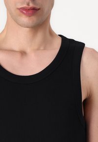 Zwarte geribbelde tanktop met een ronde halslijn en brede schouderbanden. De stof lijkt gestructureerd en sluit goed om het lichaam.