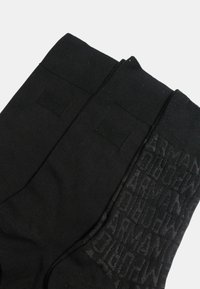 Sorte bomuldssokker med en glat tekstur og logomønster på den ene side. Den anden side er ensfarvet sort uden logoer.