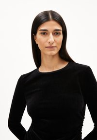 Schwarzes Samtoberteil mit langen Ärmeln und rundem Ausschnitt sowie subtiler Textur. Verfügt über geraffte Details an den Seiten für eine taillierte Optik.