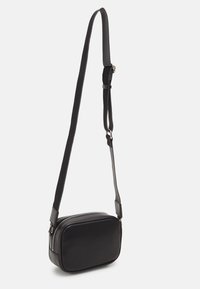 Černá crossbody taška s obdélníkovým tvarem, vyrobená z hladké kůže, s uzavíráním na zip a plochým nastavitelným popruhem.