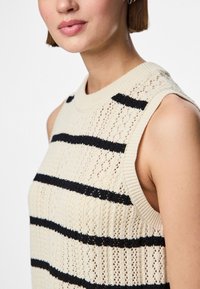 Κοντομάνικο πλεκτό τοπ χωρίς μανίκια, με εναλλασσόμενες κρεμ και μαύρες οριζόντιες ρίγες. Υφασμάτινη υφή με ανοιχτό πλέξιμο και ραμμένο λαιμό.