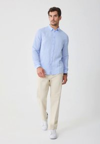 Cămașă bleu din in, cu nasturi, cu mâneci lungi, asortată cu pantaloni bej și adidași albi. Design simplu, cu guler cu rever.