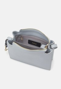 Borsa in pelle blu chiaro con una cerniera dorata. L'interno presenta una tasca e un'etichetta nera con la scritta "Furla." Texture liscia e forma strutturata.
