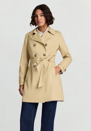 Cappotto trench doppiopetto beige con cintura annodata, grandi bottoni e tasche laterali. Tessuto liscio e design classico.