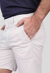 Shorts gris clair en tissu mélange coton, présentant une texture lisse, des poches latérales et une ceinture plate avec passants.