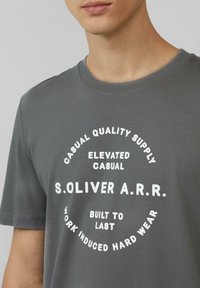 Grijze katoenen T-shirt met ronde hals, met een witte cirkelvormige grafische tekstontwerp met merknaam en slogans.