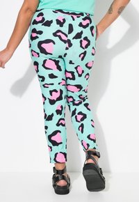 Mint green leggings with a black and pink leopard print pattern, featuring a fitted design and ending at the ankle. Adjustable black sandals shown.