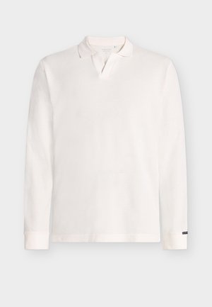 Biała koszulka polo z długim rękawem o prążkowanej fakturze, z płaskim kołnierzykiem i listwą z guzikami. Mankiety są lekko dopasowane z detalami przy krawędziach.