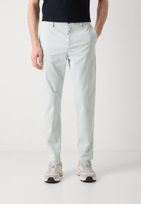Pantaloni ușori de culoare albastru deschis, cu o croială slim și buzunare standard, confecționați dintr-un material neted. Purtați cu adidași gri și bej.